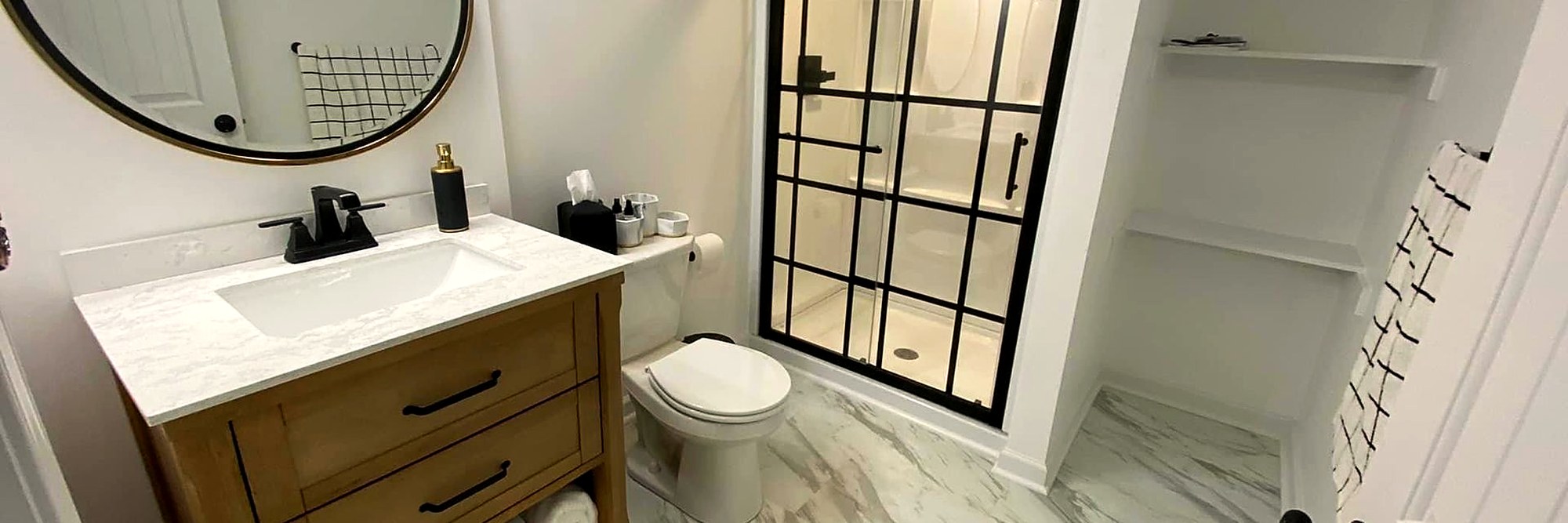 Finished lower-level bathroom with a glass shower and a round mirror.