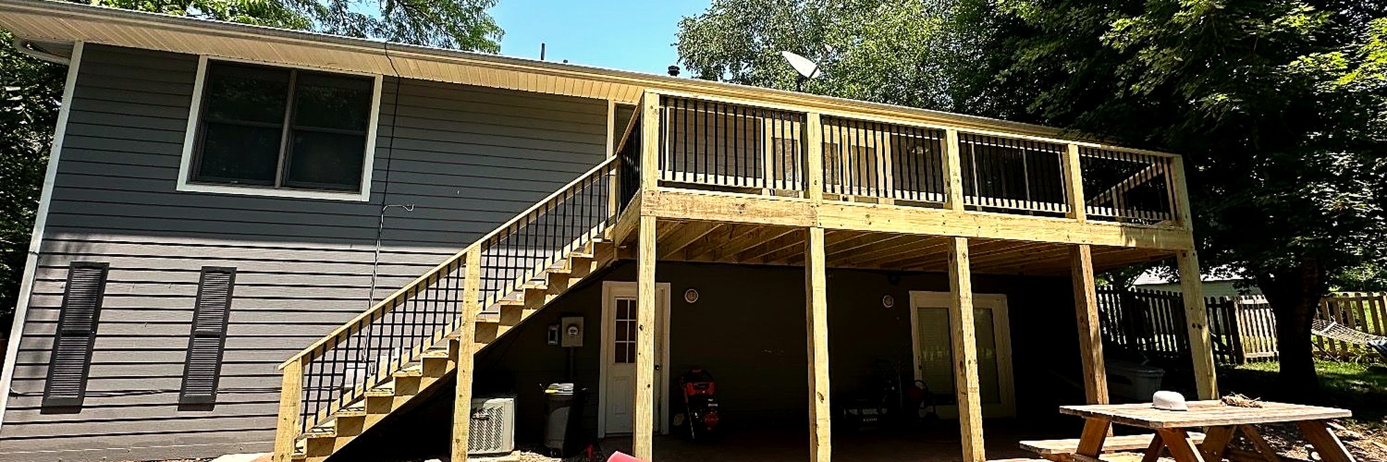 Upper deck with a pergola, seen from a lower patio with chairs.