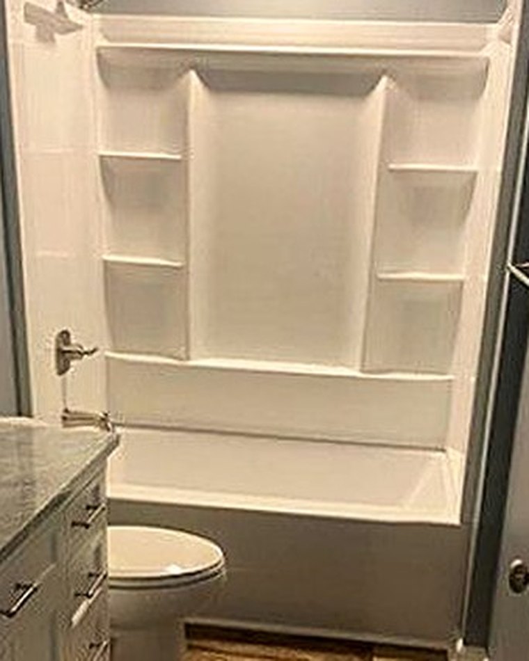 Finished bathroom with a tub-shower unit, toilet and a stone-topped vanity.