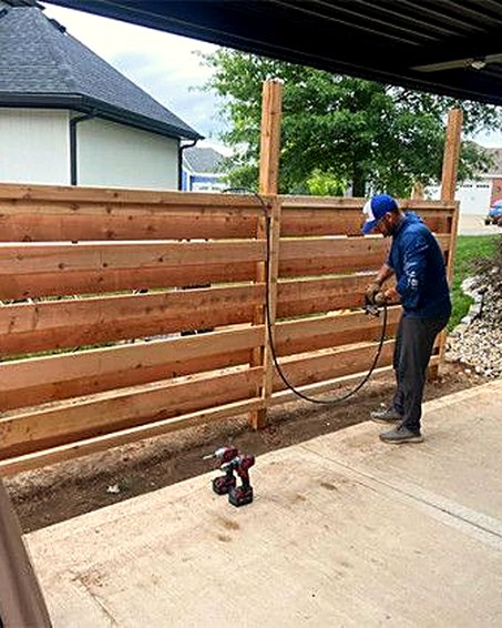 Crew member spray-staining a horizontal slat fence.