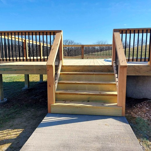 Deck with black balusters and a wide stair run down to a concrete pad.