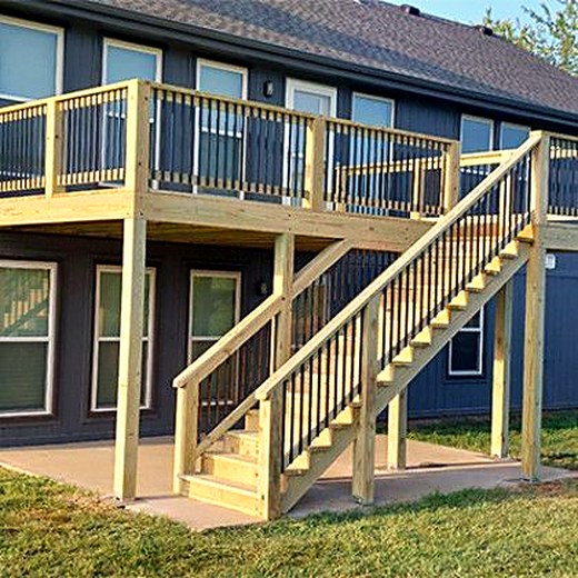 Elevated deck with cedar railings and stairs on a tan two-story home.