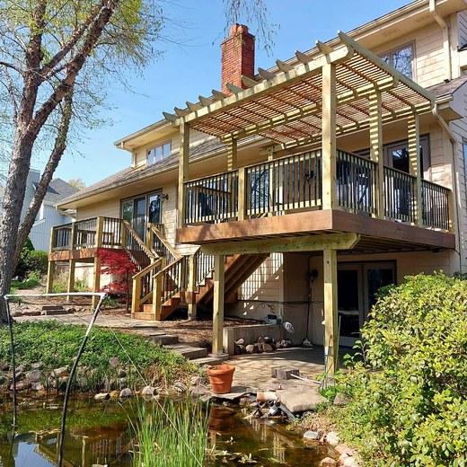 Deck with a pergola built out over a pond at the back of a home.