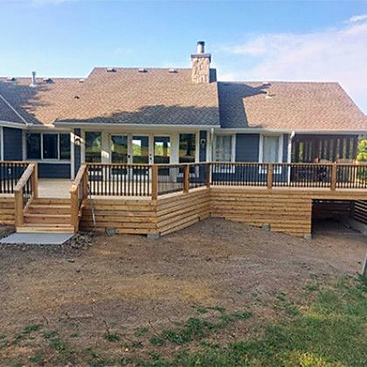 New deck and railing behind a ranch home with a freshly graded yard.