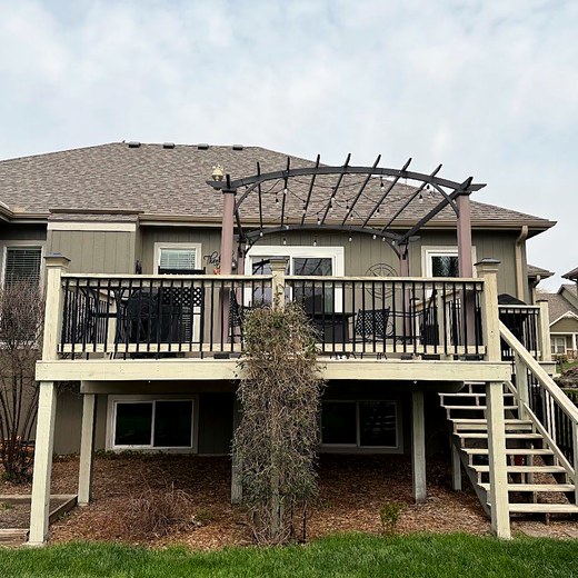 Deck with a pergola on the back of a grey two-story home.