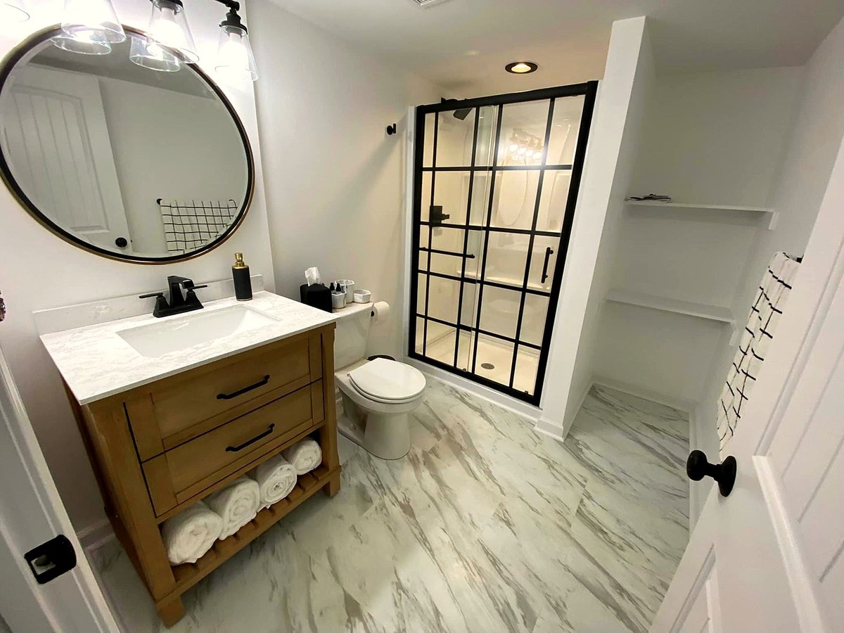 Finished bathroom with a stone-topped vanity, round mirror and a black-framed glass shower.