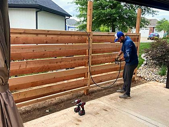 Crew member spray-staining a horizontal slat fence.